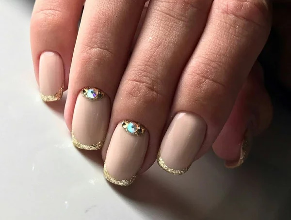 Manucure beige avec paillettes, strass sur ongles courts à la base, frottés, motif. Une photo